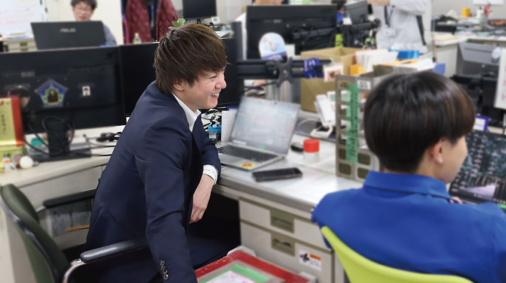 職場で営業本部の社員と談笑するREALIZEのSさん