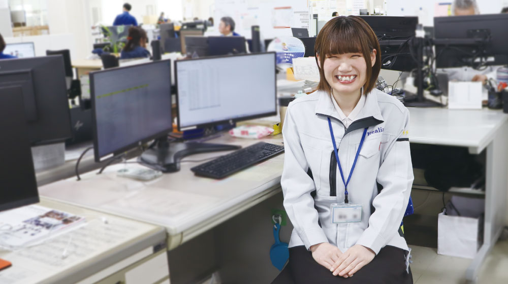 デスクの前で笑顔を見せるAさん