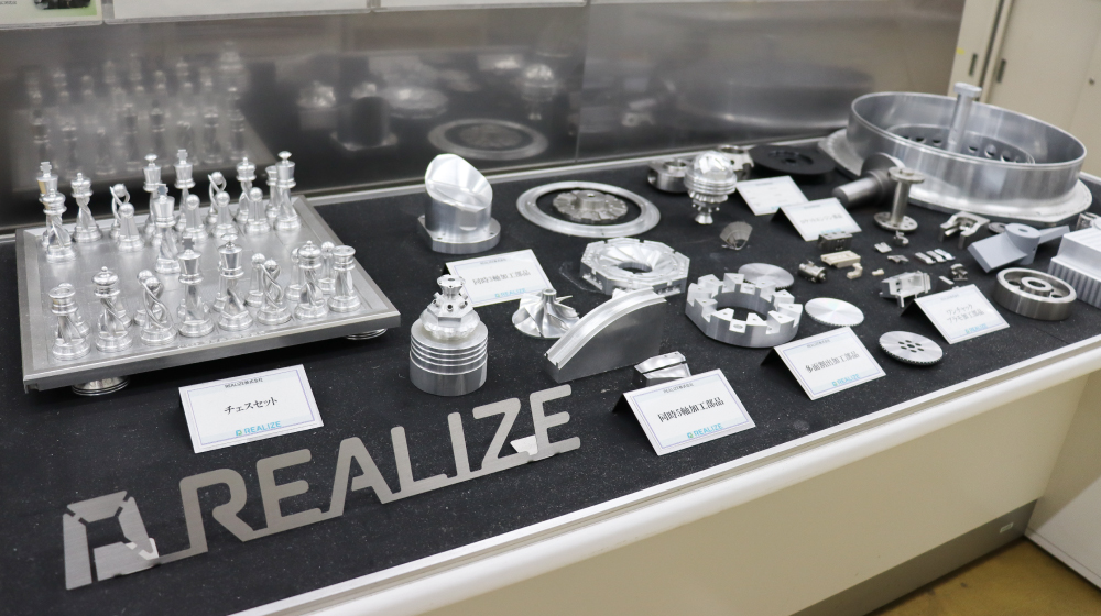 REALIZEの精密加工技術による製品展示。金属加工部品やチェスセットなどのサンプル