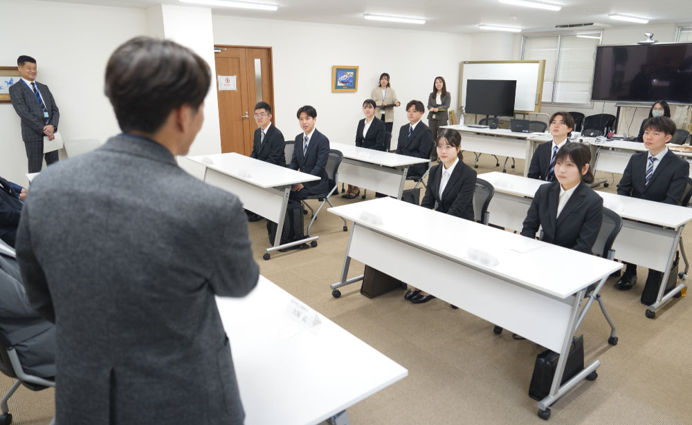 モバイルクリエイト株式会社の入社式で、役員が新入社員に向けて挨拶を行う様子。