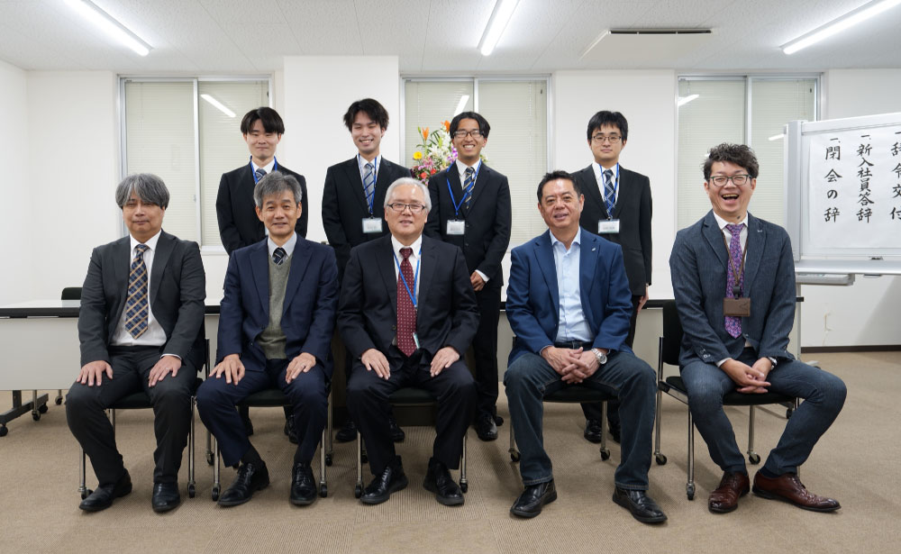 REALIZE株式会社の入社式で、役員と新入社員が並び記念撮影を行う様子。