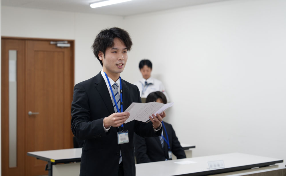 REALIZE株式会社の入社式で、新入社員が挨拶を述べている様子。