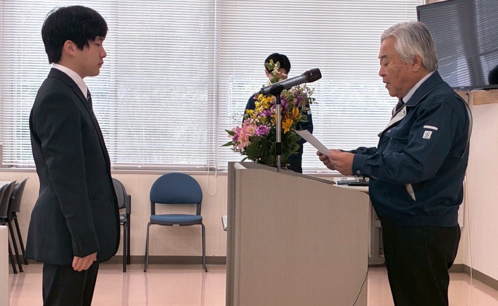 株式会社ケイティーエスの入社式で、役員が新入社員に辞令を交付する様子。