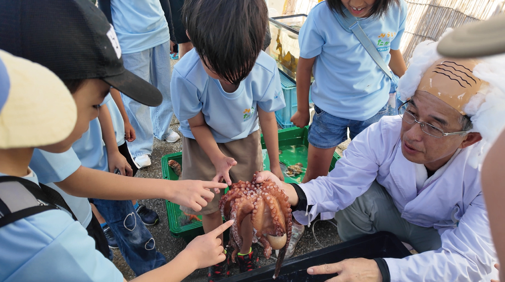 はかせの解説を聞きながらタコに触れる子どもたち