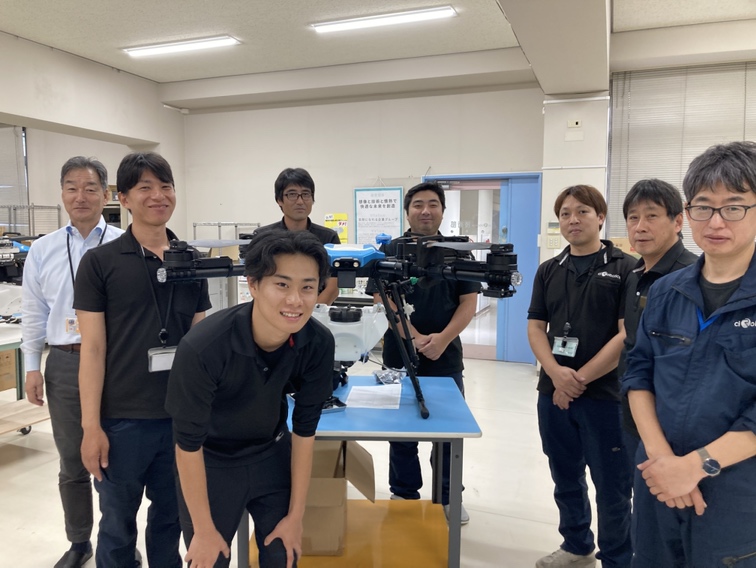 農薬散布用ドローン「R-17 V3」を囲む株式会社コバチの社員とciRoboticsの社員
